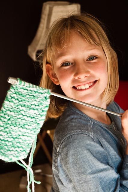 A child proudly holding a knitting needle with her first strip of knitting on it